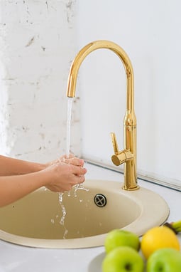 A person washing their hands with water from a golden faucet