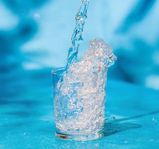 Clean water pouring and splashing into a glass cup on a blue background