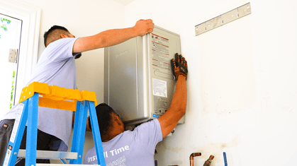 Two tankless water heater technicians placing a tankless water heater on a wall