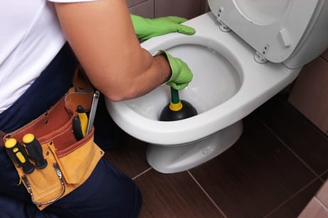 A plumber trying to clear a clogged toilet with a plunger