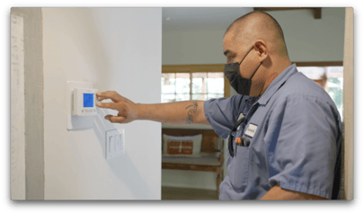 A technician from Monkey Wrench Plumbing, Heating & Air is inspecting a home's thermostat.