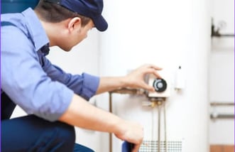 A man in blue overalls adjust the gas control knob of a conventional water heater. 