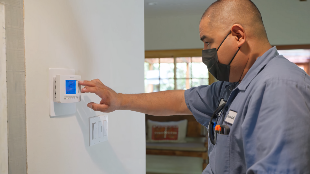 The image shows a technician adjusting the temperature on a thermostat.