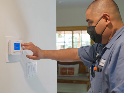 The image shows a technician adjusting the temperature on a thermostat.
