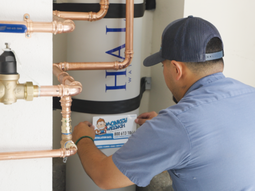 A Monkey Wrench technician placing an install sticker on a whole-house carbon filtration system.
