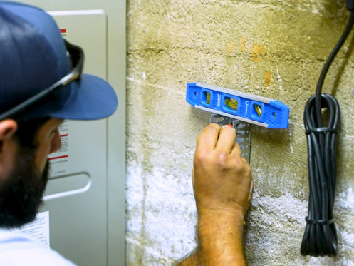 A Monkey Wrench technician is using a level meter to properly size a tankless water heater install.