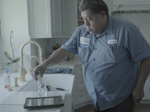 The image shows a Monkey Wrench technician testing out the hardness of water inside a home.