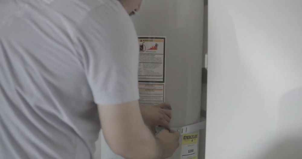 The image shows a Monkey Wrench technician tightening a screw on a conventional water heater.