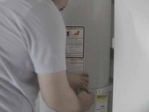 The image shows a Monkey Wrench technician tightening a screw on a conventional water heater.