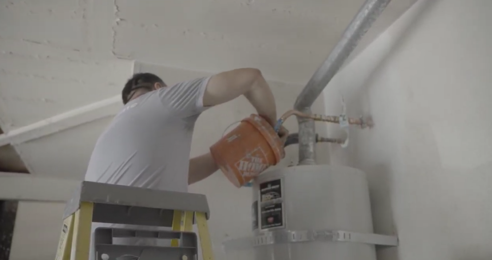 The image shows a technician performing maintenance on a conventional water heater.