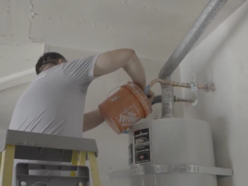 The image shows a technician performing maintenance on a conventional water heater.