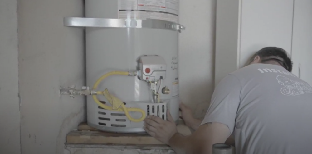 The image shows a technician from Monkey Wrench finishing up a tank-style water heater installation. 