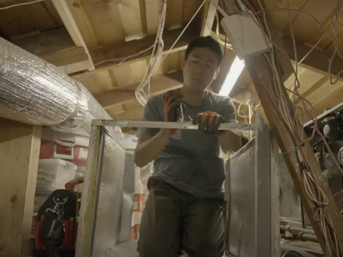 The image shows a Monkey Wrench technician using pliers on a piece of metal from an HVAC system.