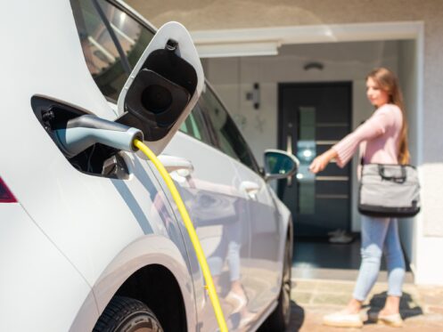 Woman charging electric car at home with cable.